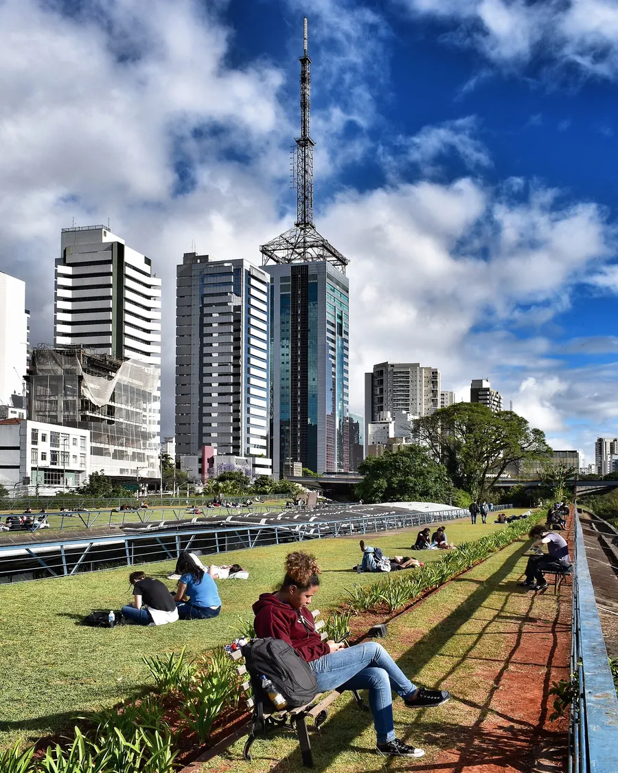 Pessoas sentadas no jardim suspenso do Centro Cultural São Paulo, com prédios da Avenida Paulista ao fundo